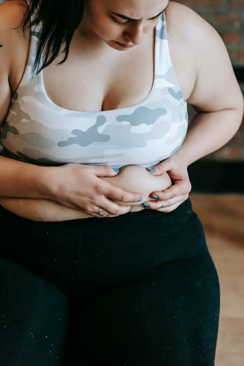 Woman in workout clothes examining her abdominal area and belly fat