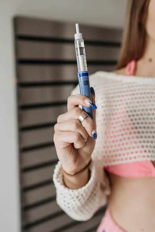 A person with blue nail polish holds up a blue and white Liraglutide pen