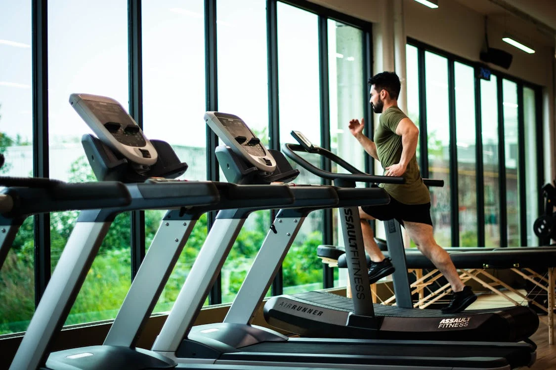 A man with a beard runs on a treadmill in a gym 