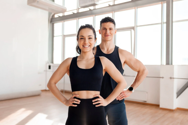 Fit man and woman standing confidently in athletic wear, smiling