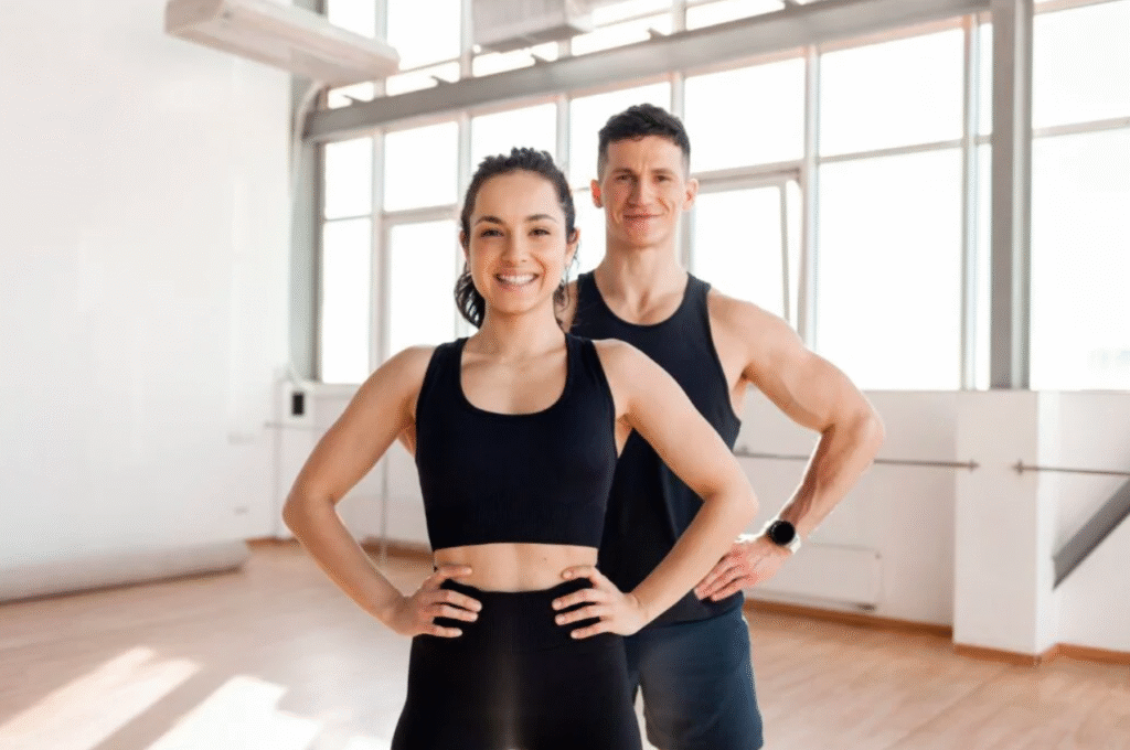 Fit, smiling man and woman standing confidently in a bright gym after achieving weight loss goals