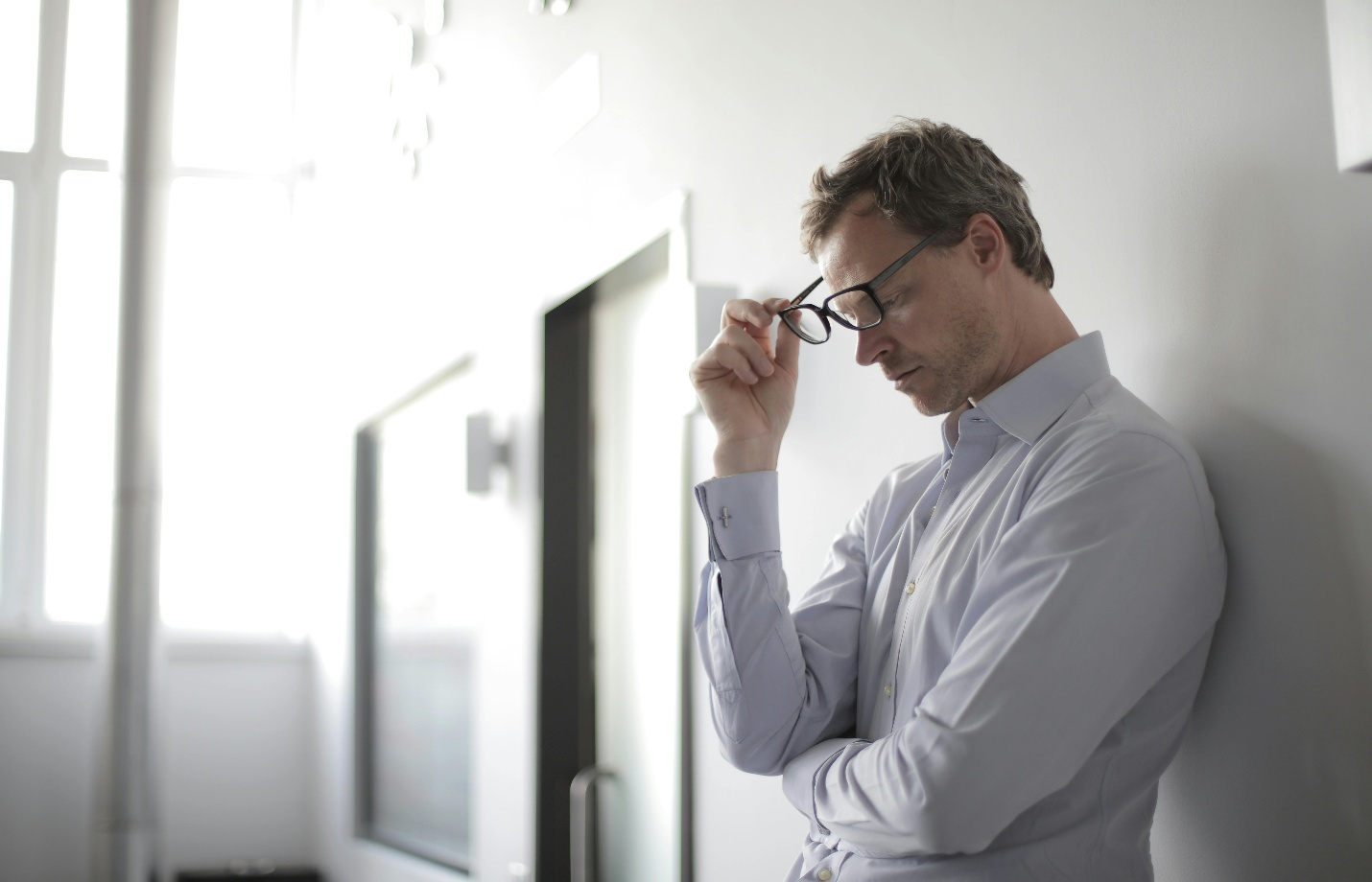 Stressed man holding glasses, showing signs of burnout and low energy