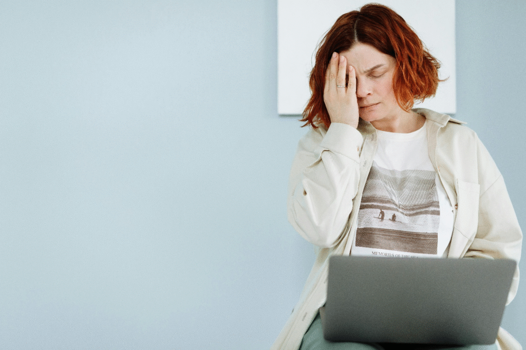 Woman feeling fatigued while using a laptop, representing burnout and energy depletion