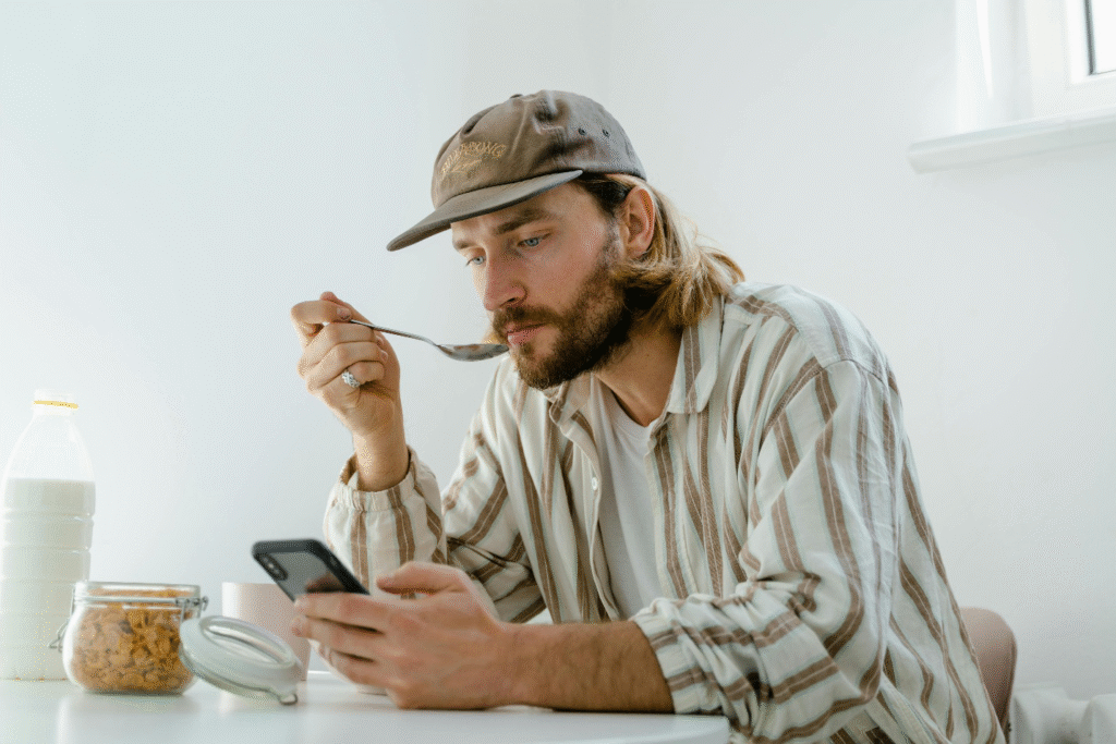 Man eating cereal while reading from his phone, reviewing health or wellness updates