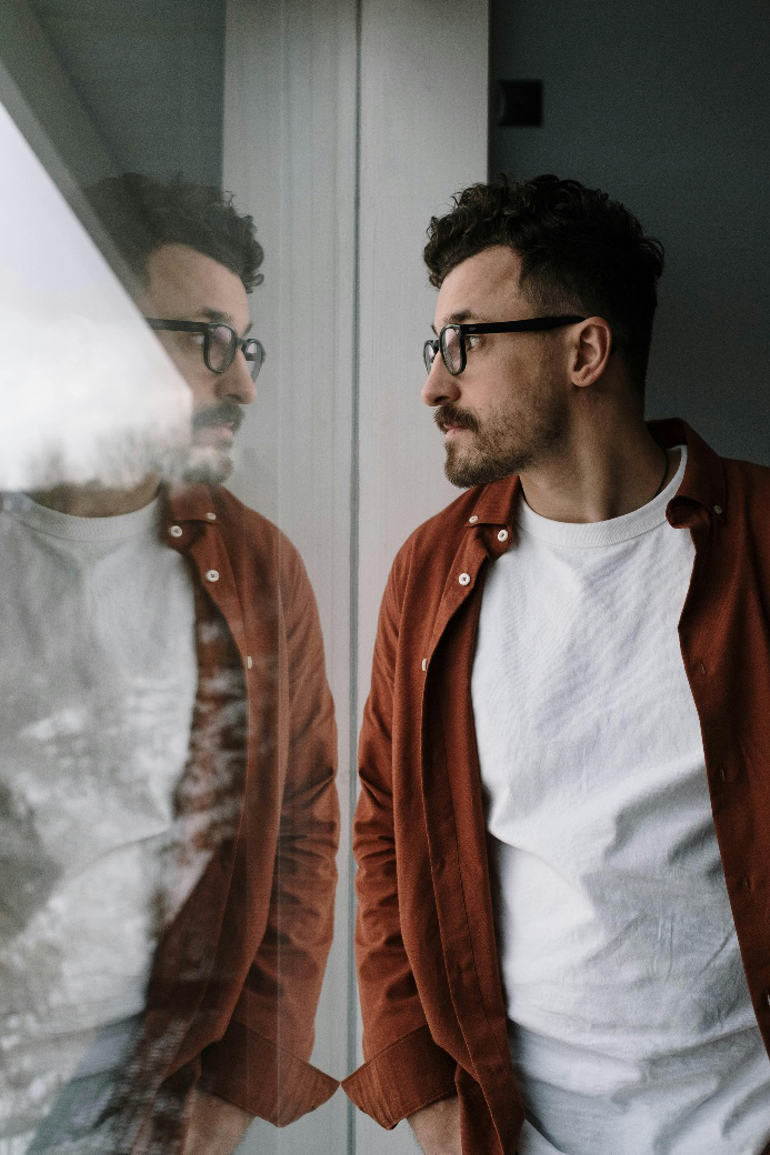 Man looking at his reflection through a window, appearing thoughtful and introspective