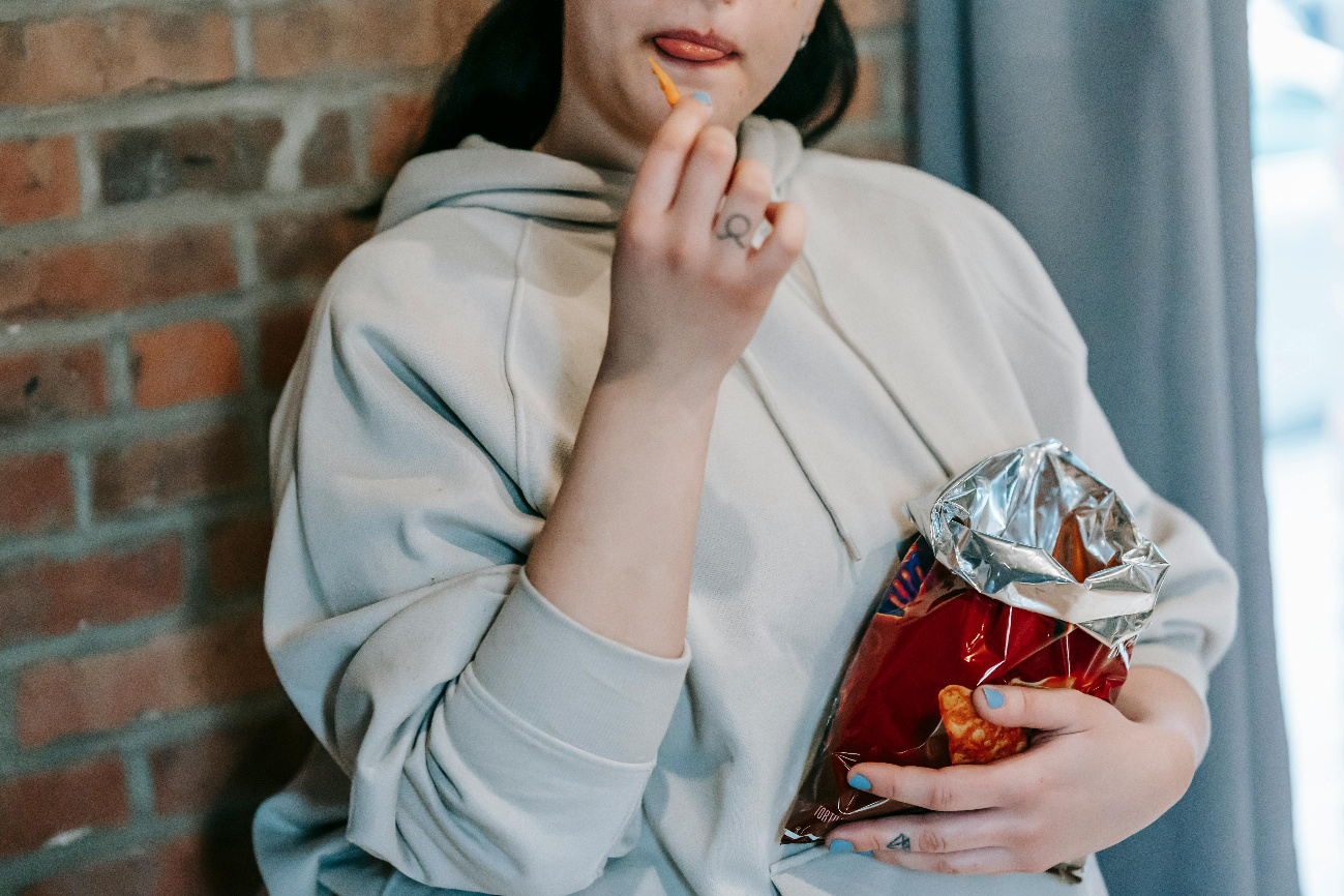 Woman eating chips from a red bag while wearing a hoodie