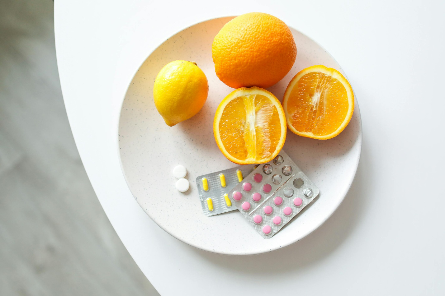 A plate with oranges, lemons, and assorted oral vitamin pills