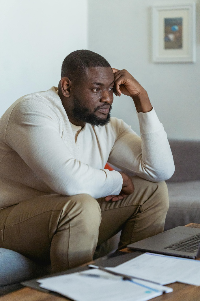 Concerned man staring at laptop with papers in front of him