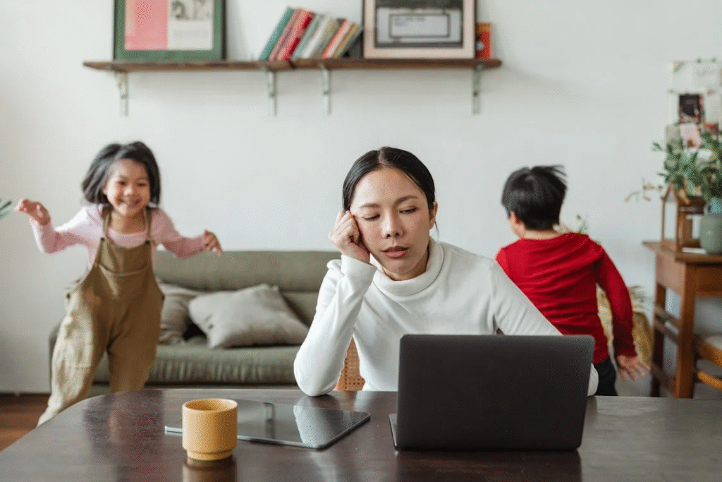 An image of a woman looking at a laptop as kids play in the background