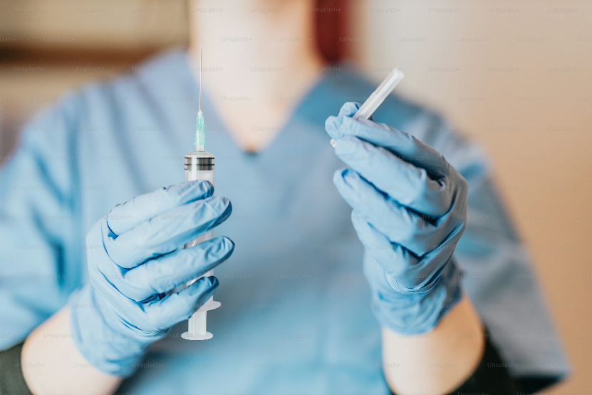 An image of a person wearing blue gloves and a robe holding an injection