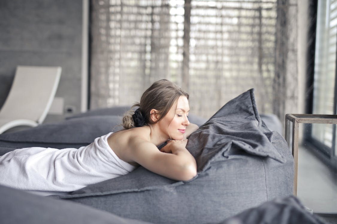 a woman relaxing on top of gray sheets.