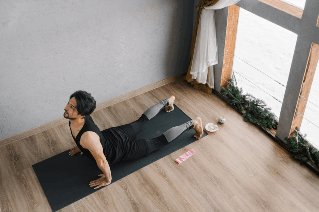 An image of a man in a black tank top doing yoga at home