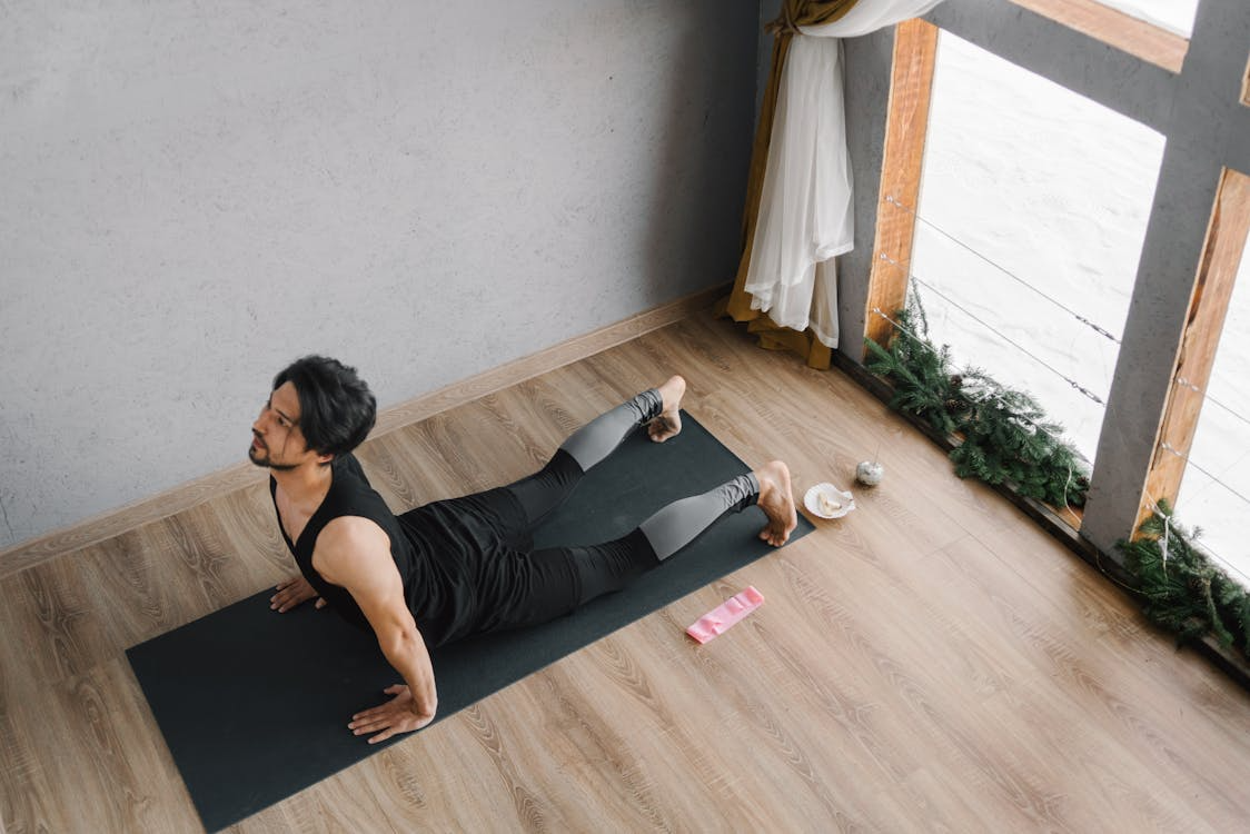 An image of a man in a black tank top doing yoga at home