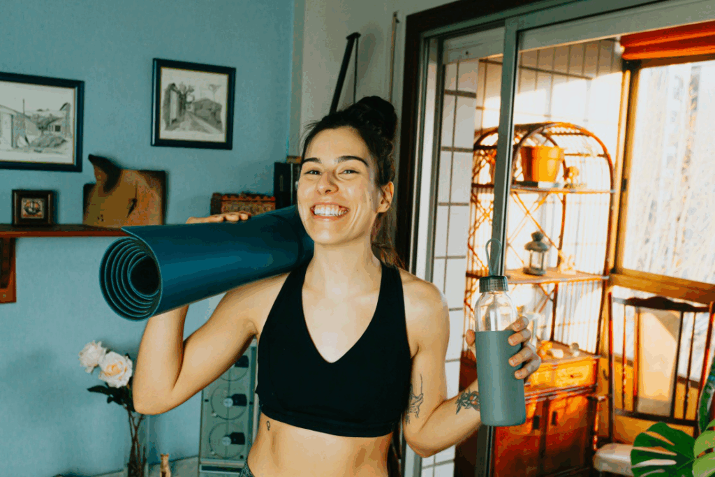 A photo of a smiling woman holding a yoga mat and a water bottle