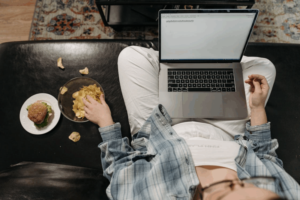 An image of a woman eating chips while working on a laptop    