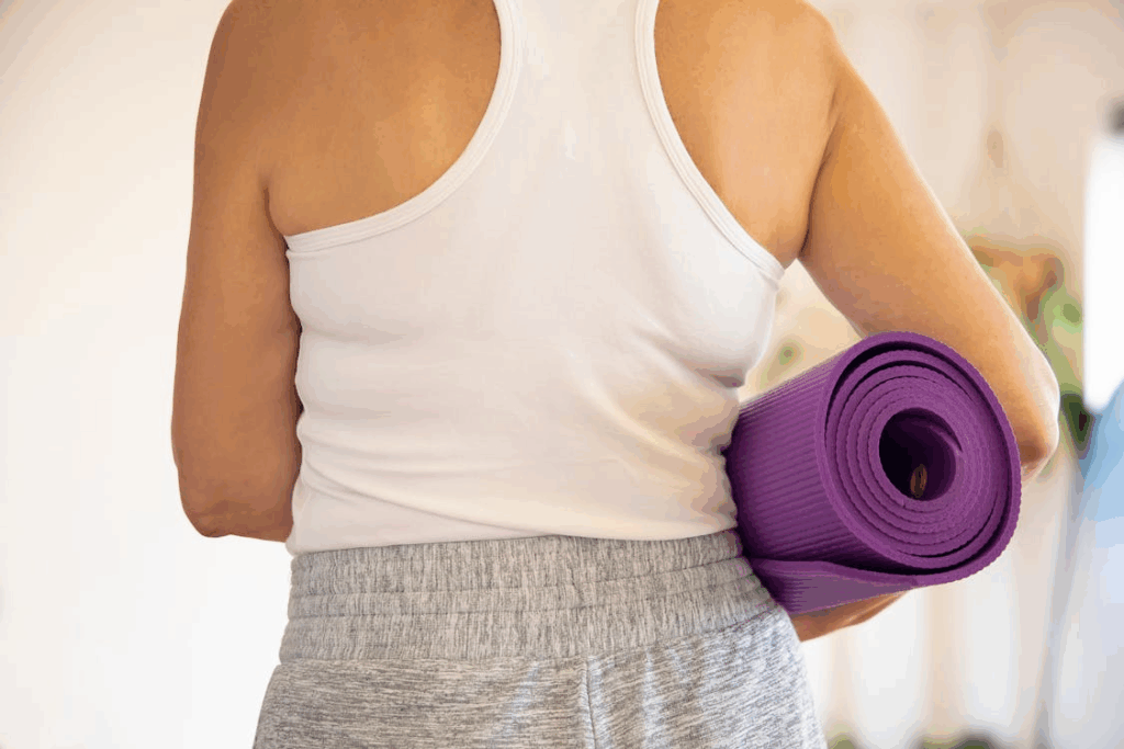 An image of a woman in a white tank top holding a purple yoga mat in her arms