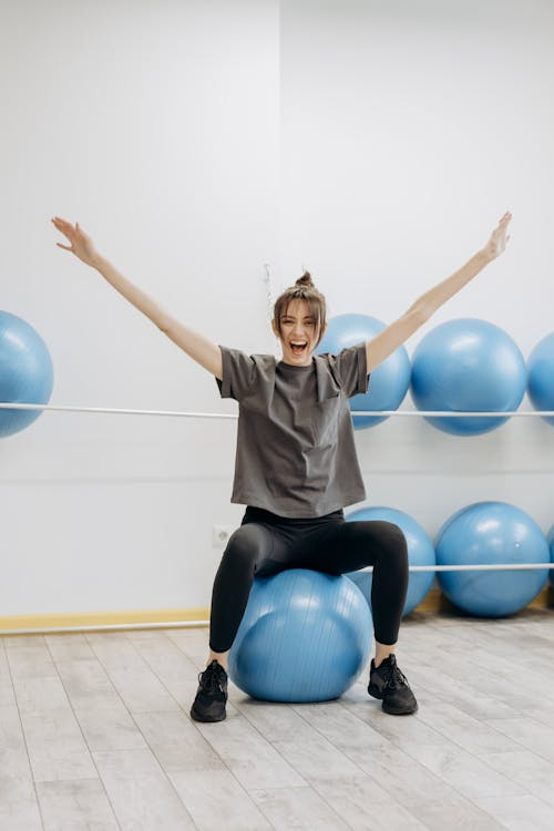 An image of a woman sitting on a yoga ball with her arms up