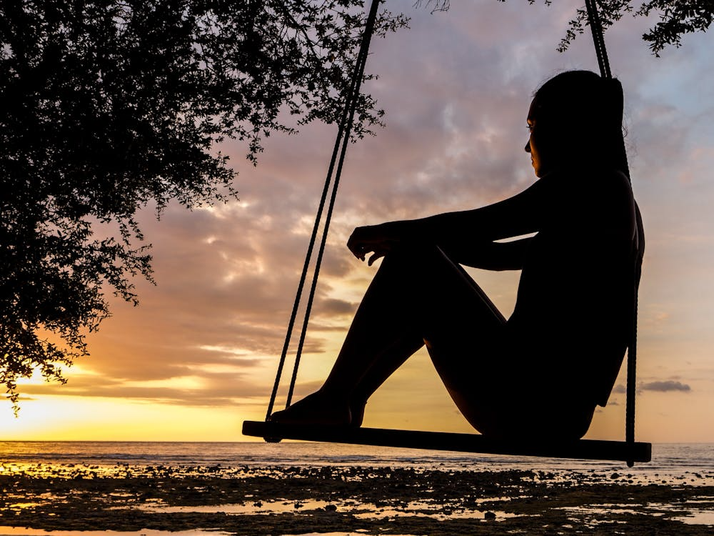 A woman sitting on a swing near the beach.
