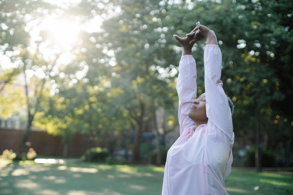 a person stretching arms wide outdoors in morning sunlight