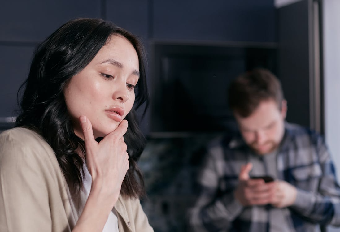 Woman looking thoughtful while a man uses a phone in the background