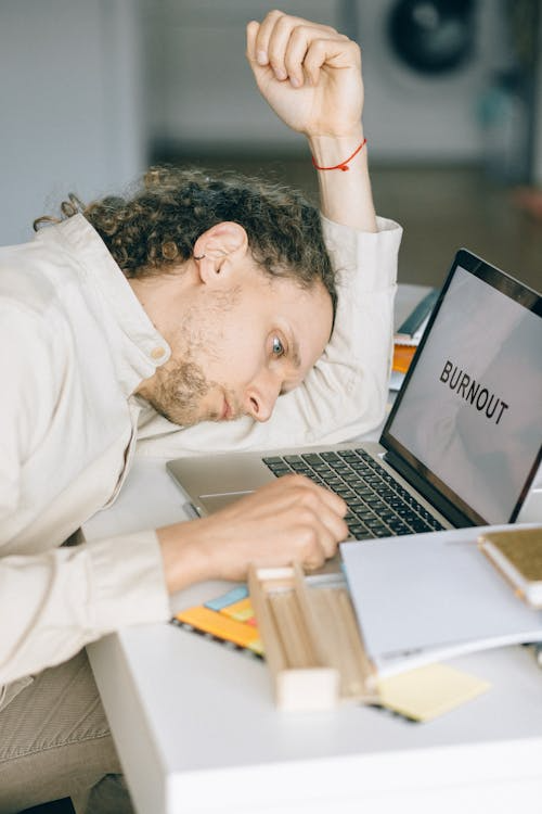 Man lying beside a laptop displaying the word burnout