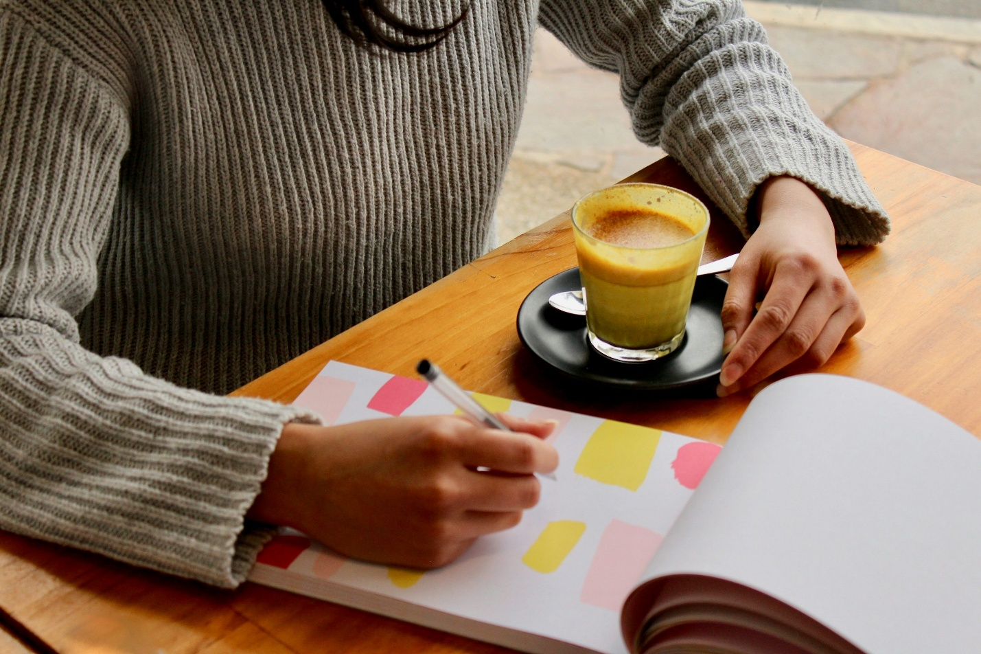 Person writing in a notebook beside a drink
