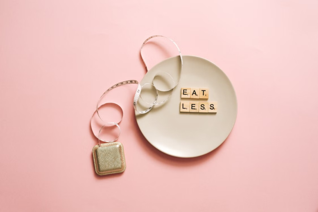 Scrabble tiles spelling "eat less" on a white plate next to a measuring tape on a pink background