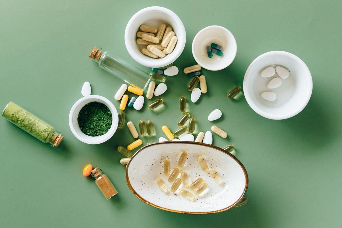 Assorted supplement capsules, tablets, and powders arranged in bowls on a green surface