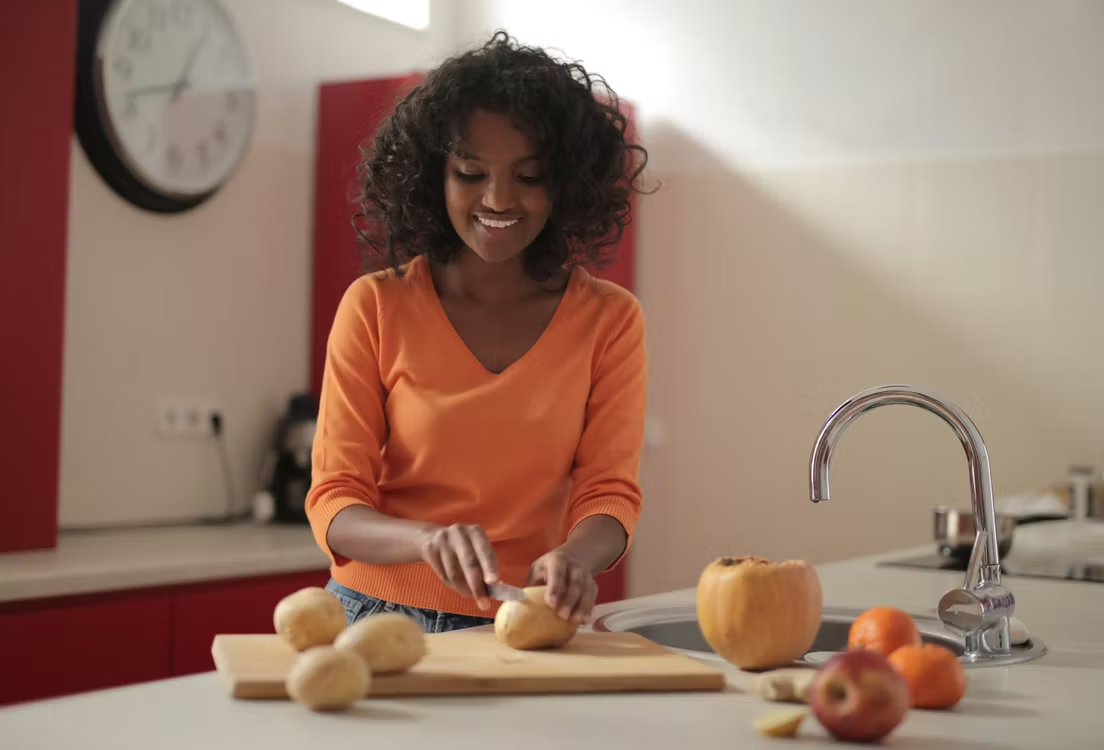 A woman in the kitchen cutting potatoes. 