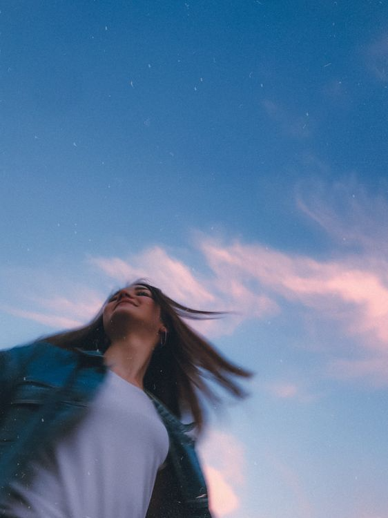 Woman looking up with windblown hair against a blue evening sky