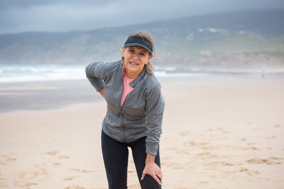 Woman standing on a beach holding her lower back