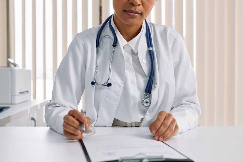 Doctor in a white coat holding a clipboard and pen at a desk