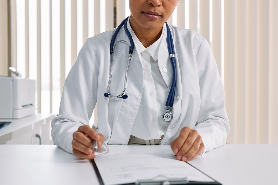 Doctor in a white coat holding a clipboard and pen at a desk