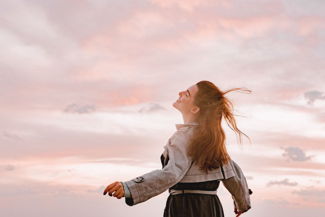 Woman with arms outstretched and hair blowing against a pink sunset sky