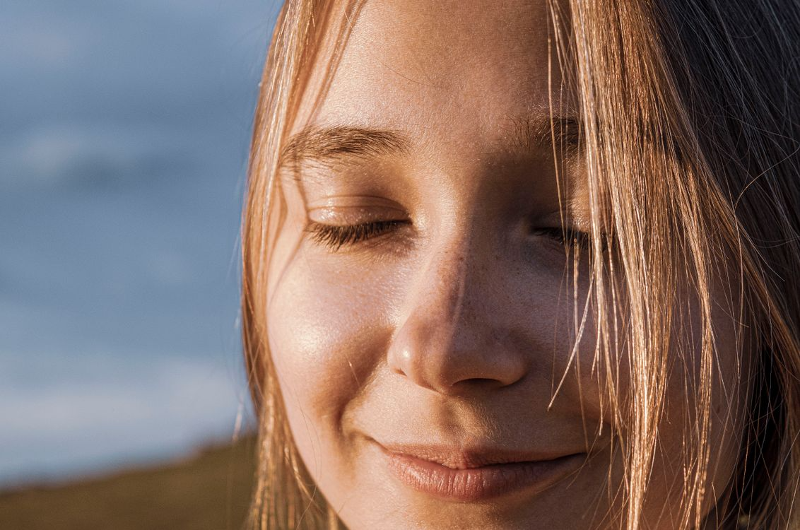 Close-up of a woman smiling with sunlight on her face and hair blowing across it