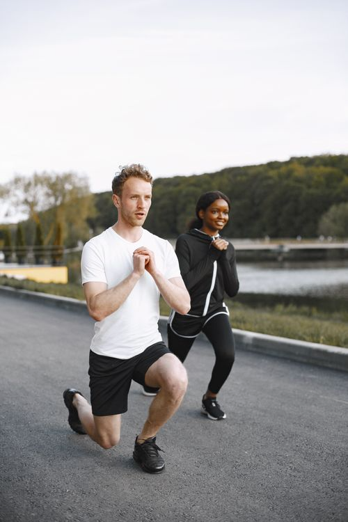 Man and woman performing lunges together outdoors near a waterfront path
