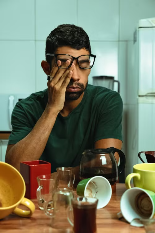 Man rubbing his eyes at a table surrounded by empty coffee mugs and glasses
