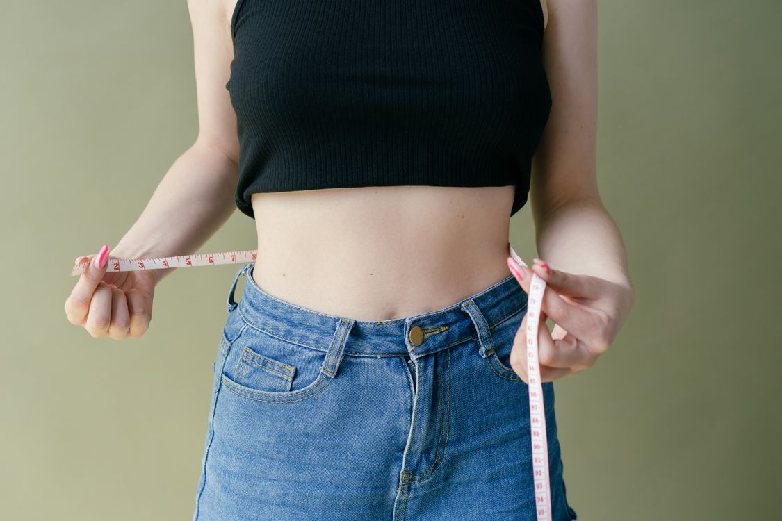 Woman measuring her waist with a pink tape measure while wearing jeans
